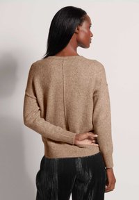 Brauner Strickpullover mit lockerer Passform, gerippten Bündchen und einer dezenten Textur. Die Rückseite hat eine Mittelnaht und wird mit plissierten schwarzen Hosen kombiniert.