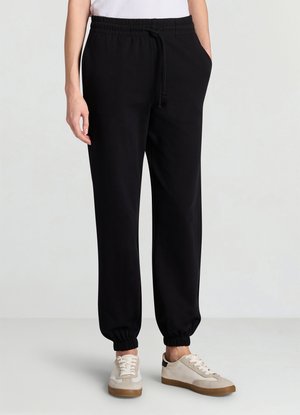 Pantaloni jogger neri con vita e polsini elastici, dotati di tasche laterali. Indossati con scarpe da ginnastica color crema e una maglietta bianca.