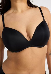 Senza cuciture, reggiseno nero con design a V profonda, spalline sottili e texture liscia. Nessun motivo o hardware visibile.