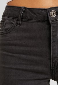 Jeans de mezclilla negros con una textura suave, con cierre de botón, bolsillo frontal y trabillas en la cintura. Vista en primer plano de la tela.