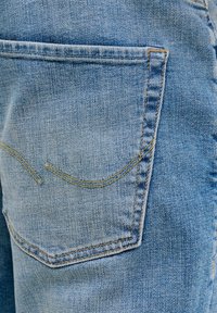 Κοντινή λήψη πίσω τσέπης από ανοιχτό μπλε τζιν με κίτρινη ραφή που αναδεικνύει την υφή του υφάσματος.