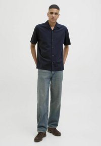 Camisa de botones de manga corta en color azul marino con collar, combinada con jeans de corte recto de lavado claro y zapatos marrones. Tejido suave, ajuste casual.