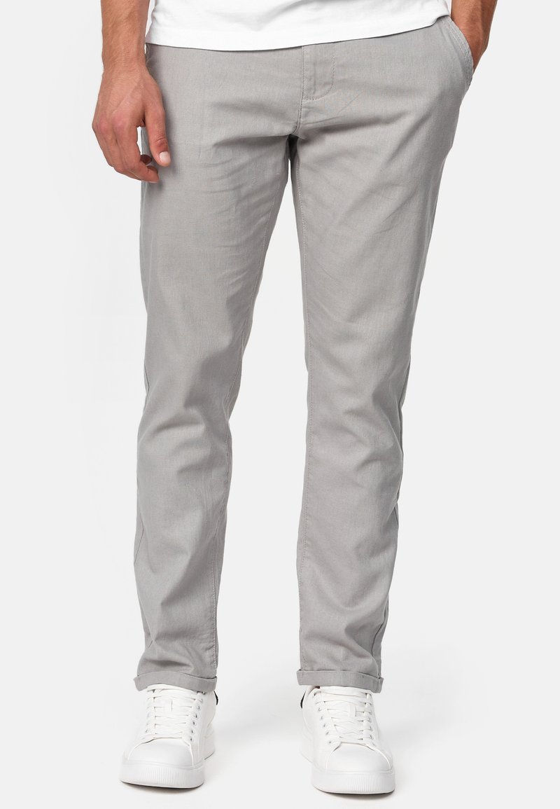 Pantalones de algodón gris claro con un ajuste slim, diseño de pierna recta y bolsillos laterales, combinados con zapatillas blancas para un look casual.