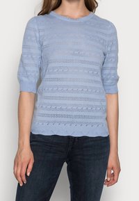 Maglione azzurro chiaro lavorato a maglia con scollatura rotonda, maniche a tre quarti e strisce testurizzate orizzontali e verticali. Dettaglio con orlo scallop.