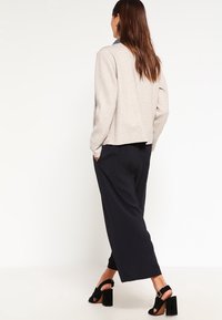 Beige skræddersyet blazer med lange ærmer, parret med løstsiddende marineblå bukser. Sorte blokhælede sandaler fuldender outfittet.