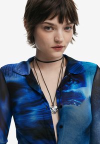 Blue patterned sheer shirt with a collar, featuring abstract designs. It's layered over a black choker necklace with a decorative silver pendant.