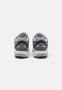 Granatowe i szare sneakersy wykonane z siateczki i zamszu. Biała podeszwa, wyściełany kołnierz oraz czerwony detal logo na pięcie. Okrągły kształt czubka.