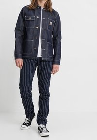 Jeansjacka i mörkblått med två bröstfickor och silverdetaljer; kombinerad med marinblå randiga byxor och svarta lågskor.