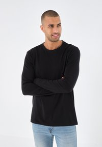 Black long-sleeve t-shirt made of a smooth fabric. Features a round neck and relaxed fit, paired with light blue jeans.