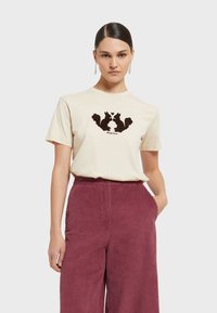 Krémové bavlnené tričko s grafikou hnedého veveričky v strede. Spárované s širokými bordovými kordúrovými nohavicami s vreckami.