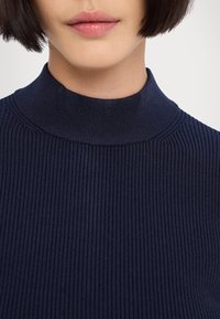 Pull à col roulé côtelé bleu marine avec une silhouette ajustée, doté d'un col haut et d'un tissu texturé, offrant un fit snug et confortable.