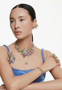 Conjunto de joyería floral colorido que presenta múltiples piedras preciosas en rosa, azul, verde y dorado. Incluye pendientes, collar, pulsera y anillos.