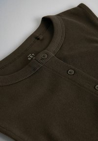 Camiseta henley de canalé marrón oscuro con escote redondo y tres botones en la parte delantera, extendida en una superficie clara.