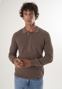 Pull en maille côtelée marron avec col polo, doté d'une patte de boutonnage et de manches longues, porté sur un jean en denim. Texture lisse.