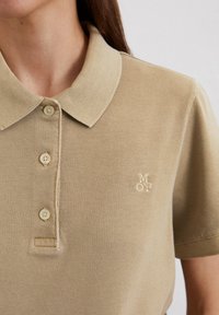 Beige poloshirt gemaakt van textiel met een gestructureerde stof, voorzien van een klassieke kraag, drie knopen aan de voorkant en een klein geborduurd logo op de borst.