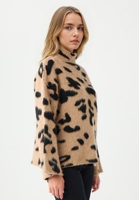 Beige coltrui gemaakt van zacht gebreid materiaal, met grote zwarte luipaardprintpatronen, verlaagde schouders en een relaxte pasvorm.
