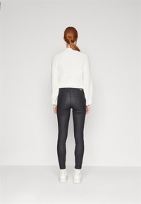 Suéter blanco de punto con hombros caídos, combinado con jeans ajustados negros y zapatillas deportivas blancas de plataforma. Fondo liso.