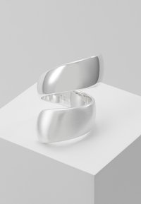 Adjustable silver-tone ring with a smooth, polished finish. Features a continuous twist design, creating a fluid shape with matte accents.
