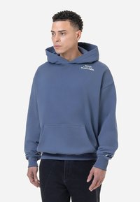 Kék kapucnis pulóver, pamut anyagból, oversized szabásban, elülső zsebbel, hímzett logóval a mellkasán, bordás mandzsettával és derékrésszel.