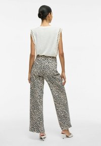 Vaaleanharmaa hihaton paita, jossa on pitsireunukset olkapäillä; leveälahkeiset housut beige- ja harmaaraidoilla; yhdistetty valkoisiin korkokenkiin.