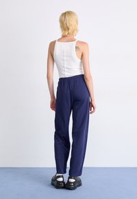Witte tanktop met een rechte snit en blauwe sweatpants met een elastische tailleband. Zwarte schoenen met een dikke zool.