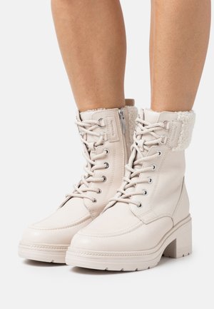White leather ankle boots featuring a plush fur cuff, lace-up design, round toe, and block heel with a textured sole for grip.