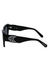 Ochelari de soare negri cu un design rectangular. Ramele din plastic lucios au un logo alb "CK" pe tâmple și o formă eleganta, minimalistă.