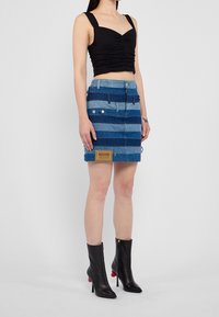 Denim minikjol med horisontella blå ränder i olika nyanser, med framknappar, fickor och en Moschino Jeans-logotyp.