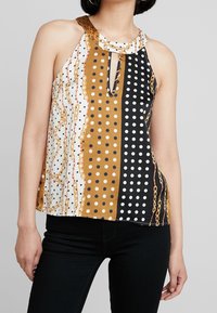 Top coloreato con scollo alla collarosso, caratterizzato da audaci pois, motivi a catena e un'apertura a forma di chiave. Realizzato in un tessuto leggero e morbido.