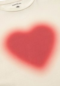 Krämfärgad T-shirt med en stor röd hjärtgrafik, med en mjuk, blandad textur och rund halsringning. "THINKING MU"-etikett synlig.