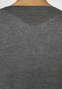 Zbliżenie na górną część pleców osoby noszącej ciemnoszary sweter z prążkowanej dzianiny z okrągłym dekoltem.