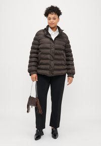 Rjav puhasti plašč z visokim ovratnikom, s horizontalnim prešitim dizajnom. V kombinaciji z črnimi hlačami in majhno rjavo torbico.