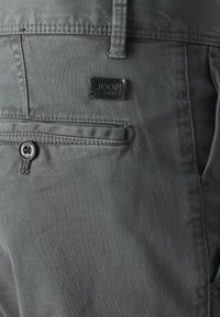 Šedé bavlněné kalhoty s zadní kapsou s černou nálepkou s nápisem "JOOP! JEANS" a odpovídajícím černým knoflíkem. Hladká textura.