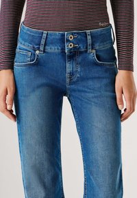 Sinised teksapüksid kitseneva lõikega, kahe-nupulise sulgemise, eest taskute ja kangal õrna kulutuse tekstuuriga.