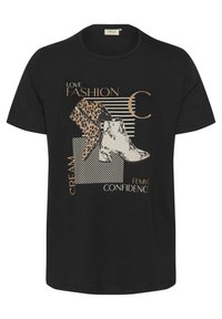 T-shirt noir avec un imprimé graphique de deux designs de bottes en motifs léopard et serpent, accentué de texte doré et de formes géométriques.