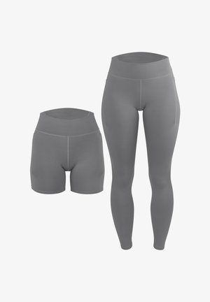 Person trägt graue Leggings mit hohem Bund und ein passendes Croptop, steht barfuß vor einem schlichten hellen Hintergrund.