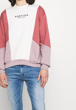 Sudadera de bloques de color en blanco, rosa y malva. Presenta cuello redondo, mangas largas y un logo en el pecho. Tejido suave con un corte relajado.