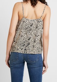 Top in beige con motivo a stampa leopardata nera, dotato di spalline sottili e regolabili, con una silhouette rilassata. Abbinato a jeans blu aderenti.