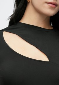 Sort topp med utskåret detalj nær skulderen. Mykt, elastisk stoff med en tettsittende passform og subtil utringning.
