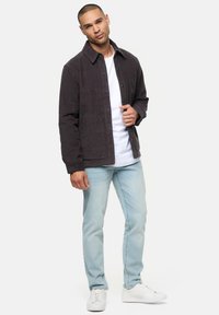 Mørk kordfløjl jakke med krave, forreste trykknaplukning og patchlommer, parret med lyse jeans og hvide sneakers.