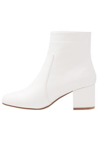 Botín blanco de tobillo fabricado en cuero suave, con puntera redondeada y un tacón cuadrado grueso. Diseño sin costuras con detalles de costura mínimos.
