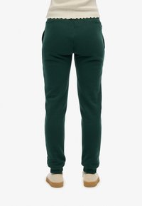Grüne Sweatpants mit schmaler Passform, elastischem Bund, Seitentaschen und gerippten Bündchen, kombiniert mit beigen Schuhen. Weicher Stoff.