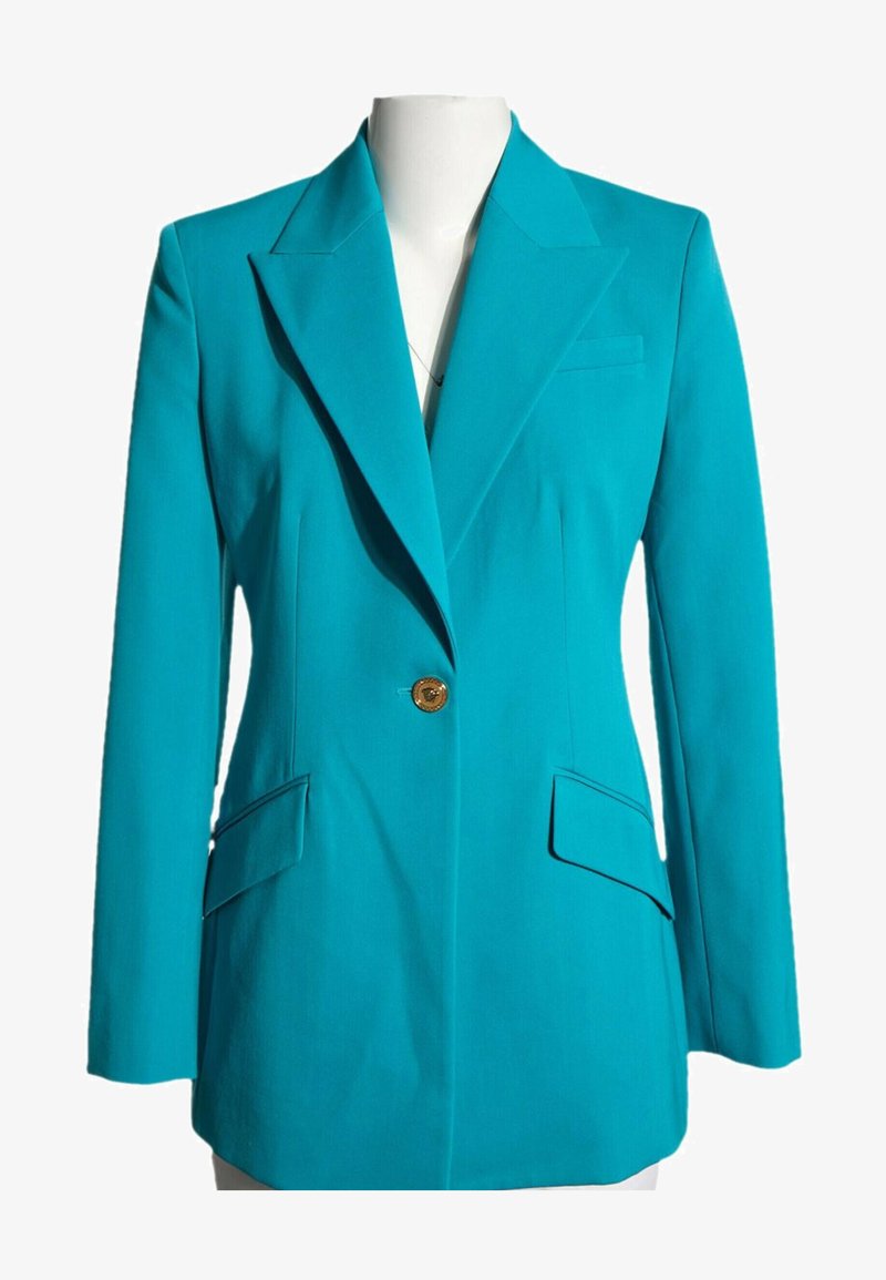 Blazer turquoise ajusté avec revers crantés, fermeture à un bouton doré, deux poches à rabat et une poche poitrine sur un mannequin blanc.