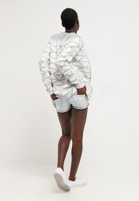 Gray and white patterned sweater with a textured finish, paired with light denim shorts and white shoes, viewed from the back.