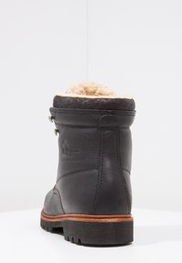 Botín negro de cuero con un suave forro de piel de oveja color beige en la parte superior, que presenta un acabado texturizado y una suela de goma con surcos.