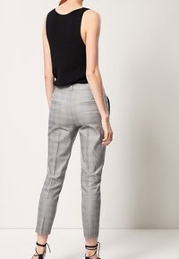 Zwarte geribbelde tanktop gecombineerd met grijze plaid tailor made broek, met een smal pasvorm, taps toelopende benen en hakken met enkelbandje.