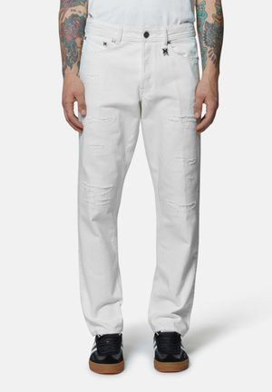 Jeans in denim bianco con toppe strappate, chiusura a bottone, passanti per cintura e vestibilità rilassata. Abbinati a sneakers nere.