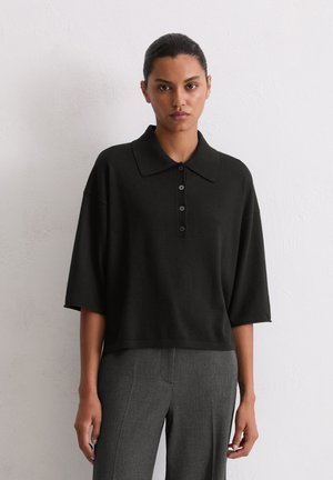 Polo top nero lavorato a maglia con colletto, dotato di bottoni e maniche corte. Abbinato a pantaloni grigi a quadri.