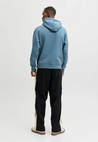 Svetle modrá mikina s volným střihem a nastavitelnou kapucí, spárovaná s černými kalhotami se smetanovými bočními pruhy a šedými teniskami.