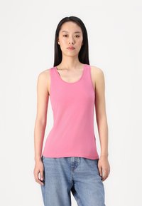Top sin mangas de color rosa en tela ligera, con escote redondo y corte ajustado. Combinado con unos vaqueros de denim azul de corte holgado.